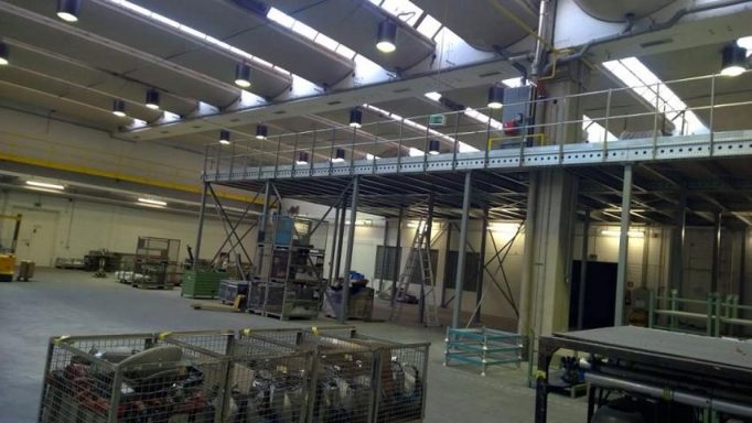 Große Lagerhalle mit Maschinen und hohem Regalsystem, gut beleuchtet.