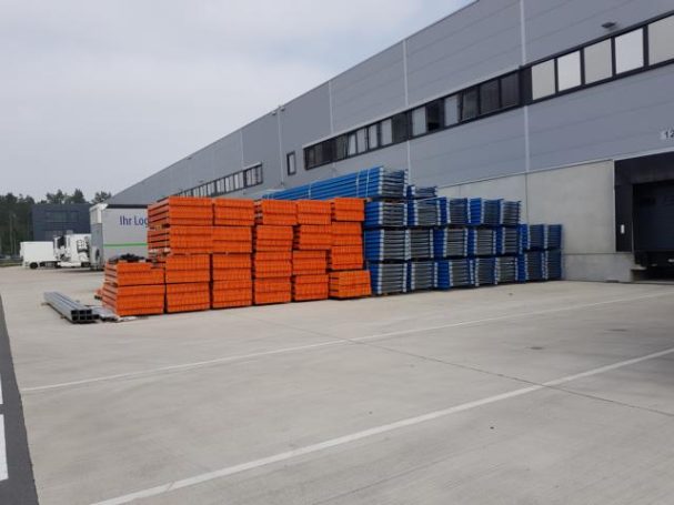 Vergatterte Fläche neben Lagerhaus mit gestapelten blauen und orangefarbenen Materialien.