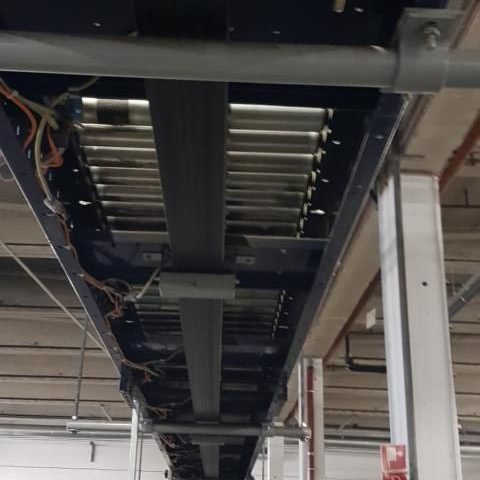 Unterseite eines Förderbands mit Rollen und Kabeln in einem Industriegebäude.