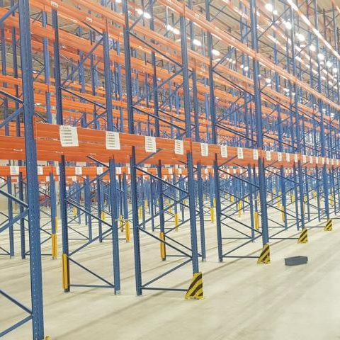 Leere Lagerregale mit orangefarbenen und blauen Ständern in einer großen Halle.