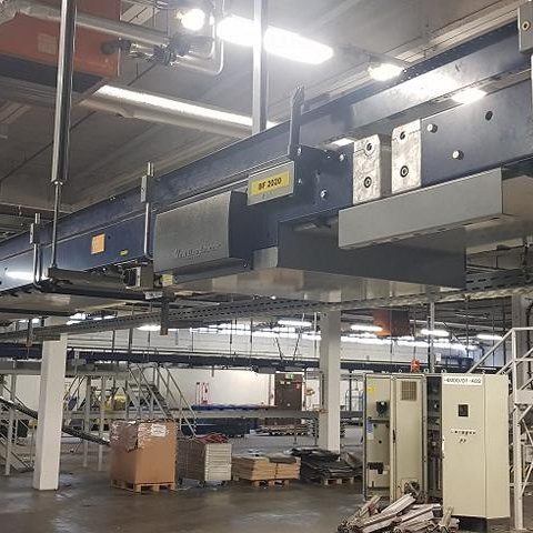 Industriehalle mit hängendem Kran und Maschinen in der Umgebung.