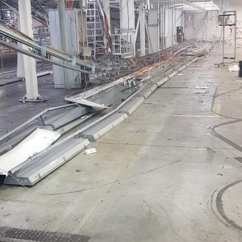 Zerstörte Produktionslinie in einer Industrieeinrichtung, mit Trümmern und Kabeln.