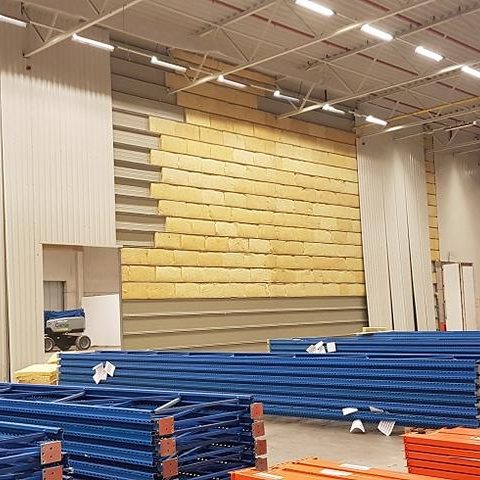 Lagerraum mit gestapelten Holzpaletten und blauen Metallregalen.