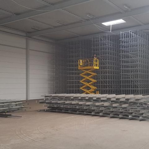 Lagerhalle mit gestapelten Metallregalen und einer Hebebühne.