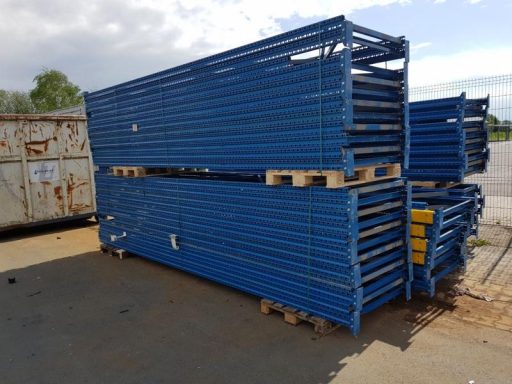 Blaue Stapel aus Metallregalen auf Paletten in einem Außenbereich.