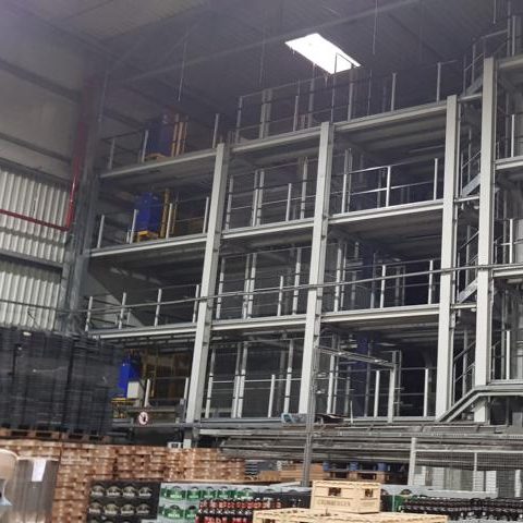 Lagerraum mit Regalen und gestapelten Paletten im Vordergrund.