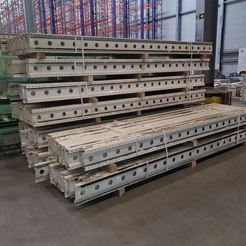 Gestapelte Metallträger auf Paletten in einem Lager.