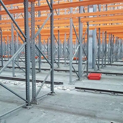 Blick auf leere Regale in einem Lager mit metallenen Stützen und orangefarbenen Balken.