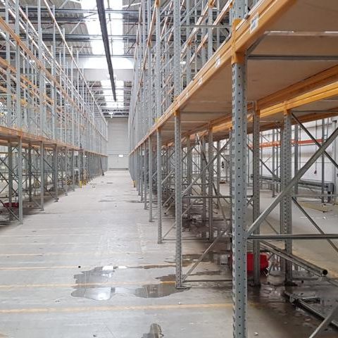 Leeres Lager mit hohen Regalen und Betonboden, schwacher Beleuchtung.