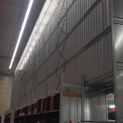 Metallische Wand mit vertikalen Streifen und hängenden Regalen im Hintergrund.