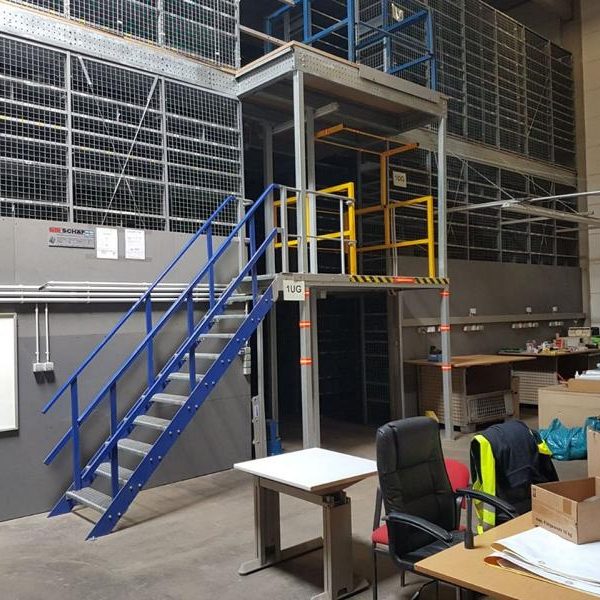 Lagerhalle mit Treppenaufgang, Regalen und Büromobiliar.