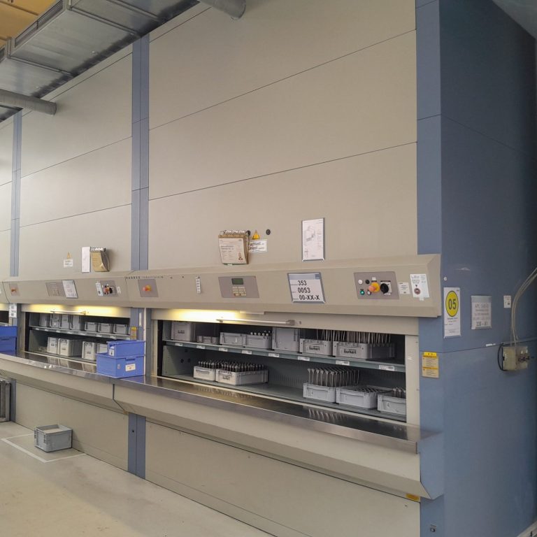 Regal mit Kästen in einer Industrieumgebung, graue Wände und Beleuchtung.