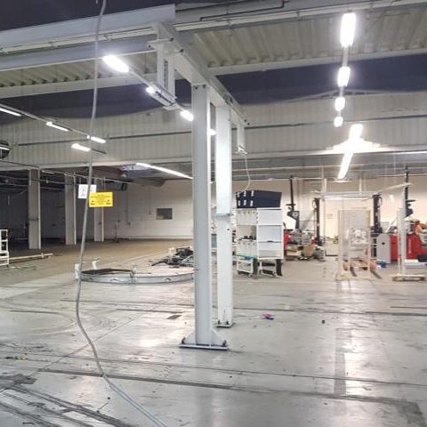 Leere Industriehalle mit hohem Deckenraum und verschiedenen Geräten und Materialien.