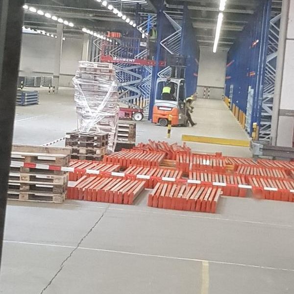 Lager mit Holzpaletten und Lagerregalen, Gabelstapler im Hintergrund.