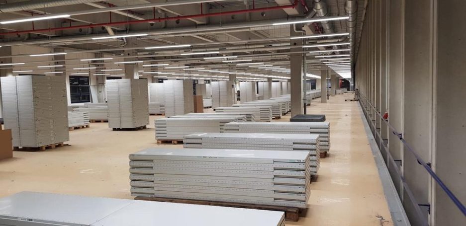 Leere Lagerhalle mit mehreren weißen Regalen und neutralem Bodenbelag.