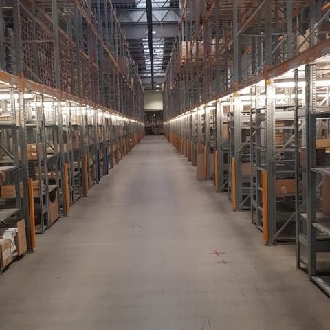 Ein langes Lager mit Regalen auf beiden Seiten, beleuchtet und gut organisiert.