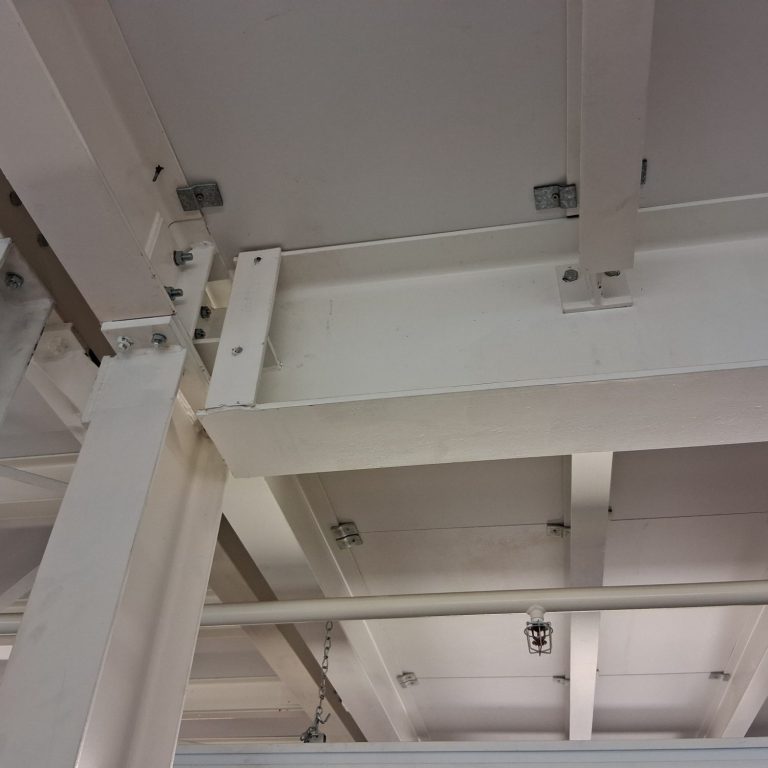 Weiße Deckenbalken und Metallbefestigungen in einem Innenraum.