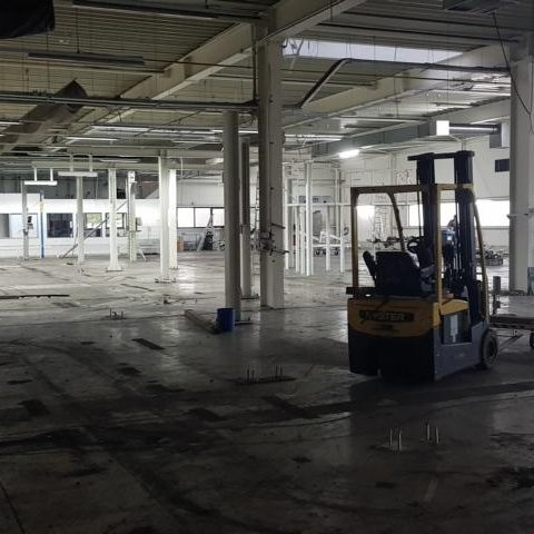 Leere Lagerhalle mit einem Gabelstapler und sichtbaren Baustellenarbeiten.