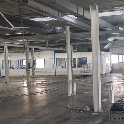 Leere industrielle Halle mit Stahlstützen und großen Fenstern.