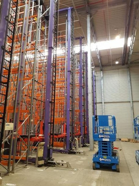 Bunte Regalsysteme in einer Lagerhalle mit Arbeitsbühne im Vordergrund.