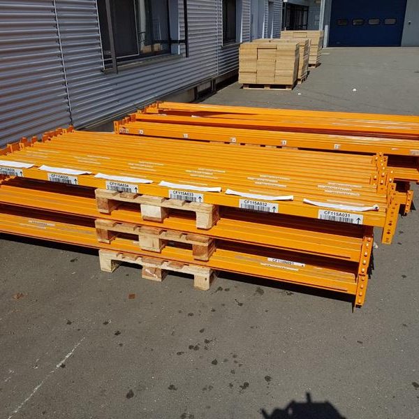 Orange Gerüstträger auf Paletten, gestapelt auf einem Betonboden neben einem Gebäude.