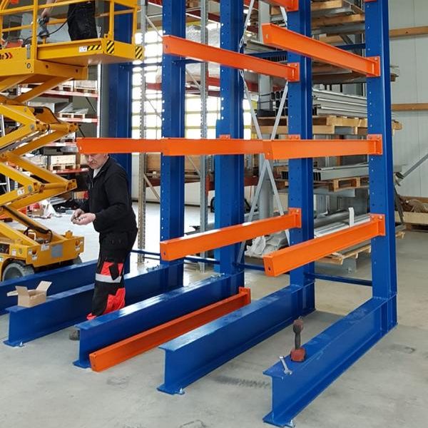 Regalsystem mit blauen und orangen Streben in einem Lagerraum, Arbeiter in der Nähe.