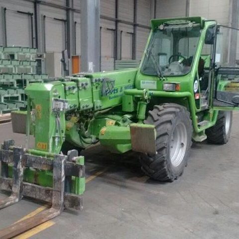 Grüner Teleskoplader mit Schaufel in einem Lagerhaus.