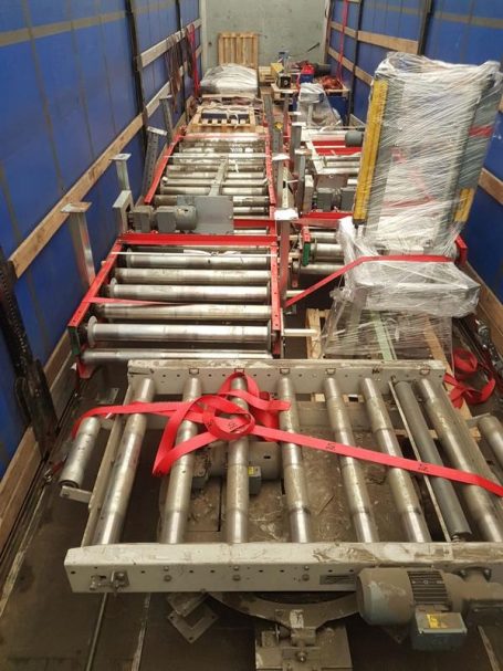 Rollenförderer und Materialien, gesichert im Lkw mit roten Gurten.