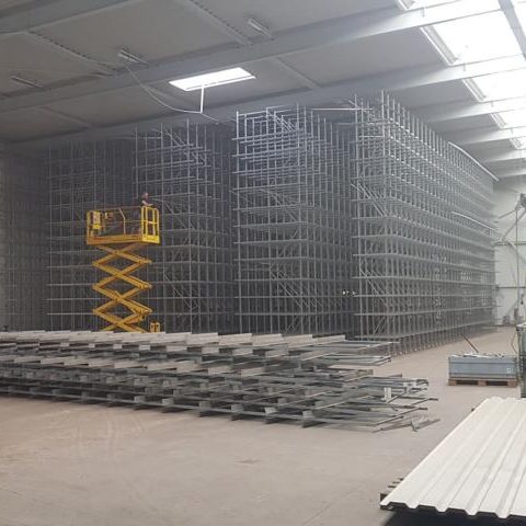 Lagerhalle mit Regalsystemen und einer Hebebühne in der Mitte.