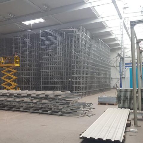 Lagerhalle mit Metallregalen und einer Hebebühne, leere Flächen auf dem Boden.