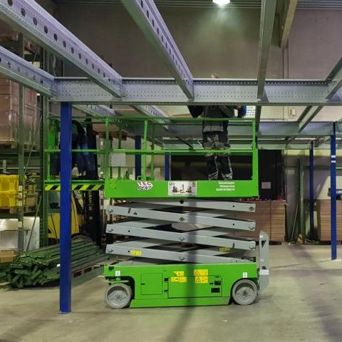 Grüner Hochhubwagen in einem Lager, unterstützt bei Regalarbeiten.