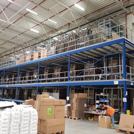Lagerhalle mit Regalen voller Kartons und einem Arbeiter am Tisch.