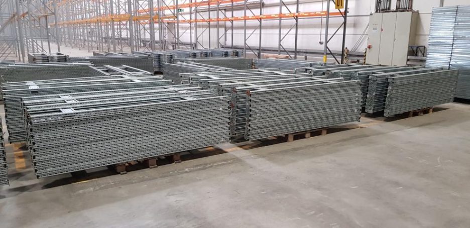 Staple von grauen Metallgestellen auf Holzpaletten in einem Lager.