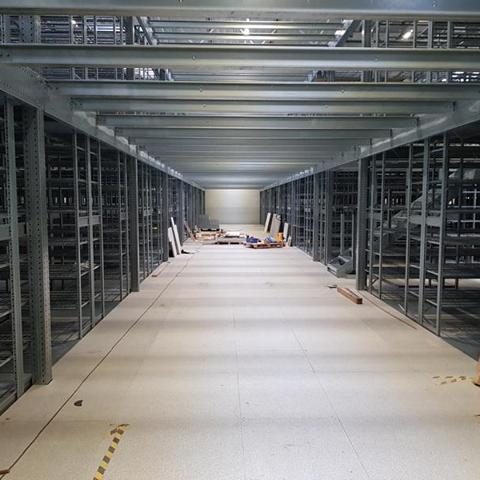 Leere Lagerhalle mit Regalen und einem Betonboden, gut beleuchtet.