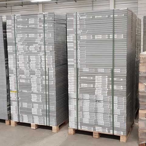 Gestapelte Paletten mit grauen Holzplatten in einem Lager.