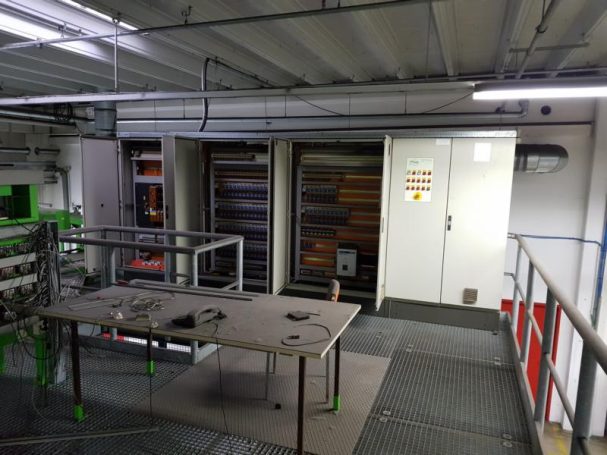 Ein Raum mit Regalen, einem Tisch und Elektrogeräten in einer industriellen Umgebung.