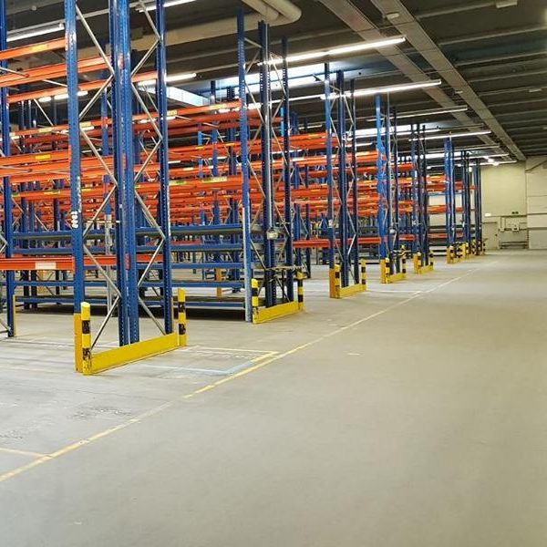 Leeres Lager mit blauen Regalen und orangefarbenen Gestellen. Bretter stehen bereit.