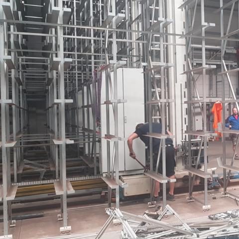 Bauarbeiter montiert Gerüst in einem Arbeitsbereich mit vielen Gerüstteilen.