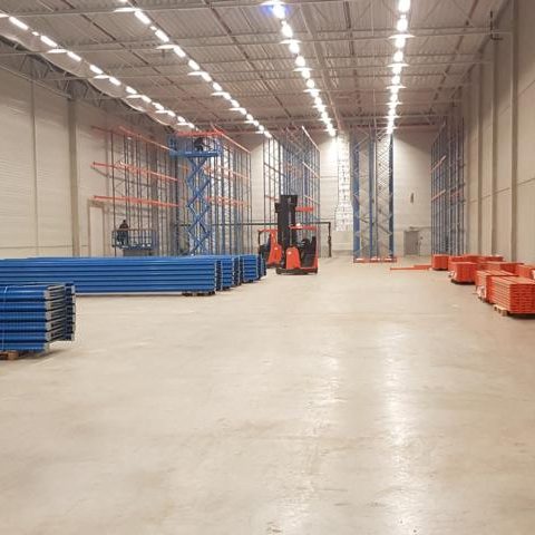 Leerer Lagerraum mit blauen und roten Regalen sowie Gabelstaplern.
