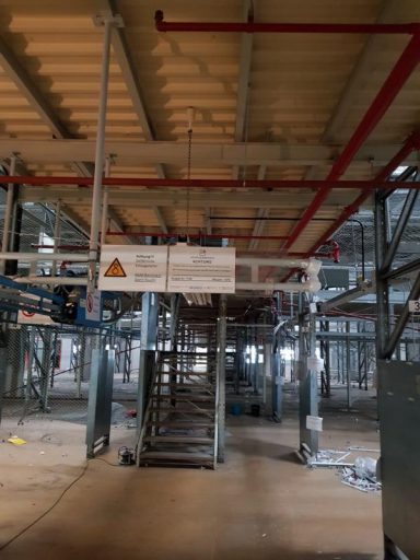 Blick auf ein Baustellengerüst mit roten Rohrleitungen und Warnschild.