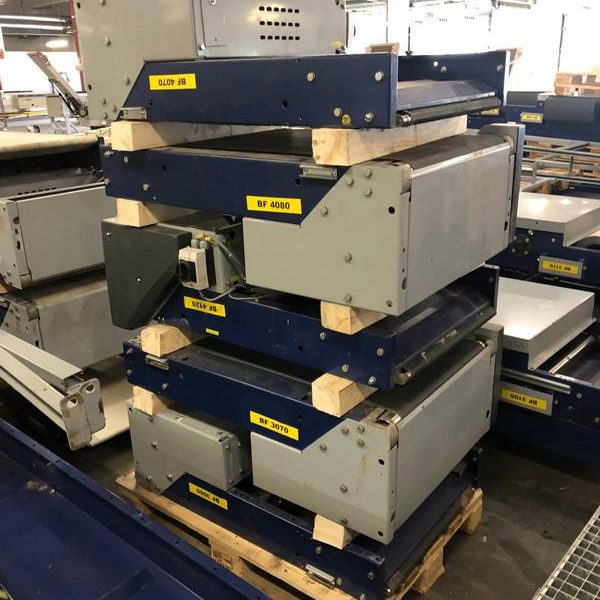 Stapelt mehrere graue und blaue Maschinenkomponenten auf Holzpaletten.