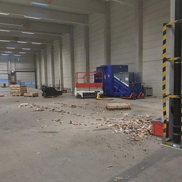Ein leerer Lagerraum mit verstreuten Holzpaletten und Maschinen in der Ecke.