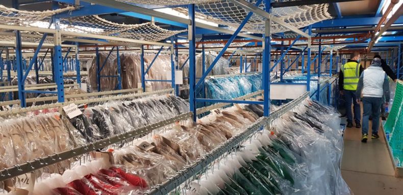 Lageransicht mit Regalen voller Verpackungen und Mitarbeitern im Hintergrund.