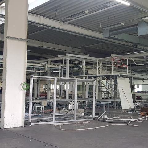 Leere Industriehalle mit Maschinenrahmen und Kabeln im Hintergrund.