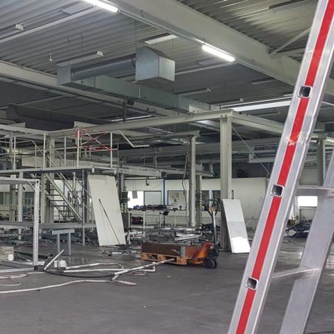 Blick auf eine leere Industriehalle mit Leitern und Maschinen.