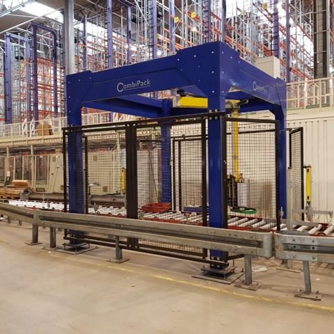 Automatisierte Verpackungsstation in einem Lager mit Förderband und Sicherheitsgitter.