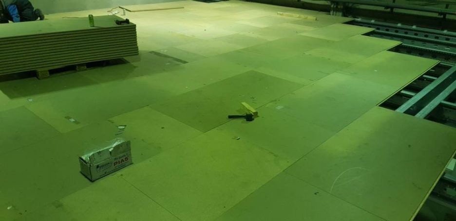 Unfertiger Boden mit mehreren Holzplatten und einem Werkzeugelement auf der Fläche.