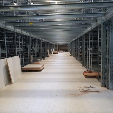 Leere Lagerhalle mit Regalen, Brettern und einem hellen Fußboden.