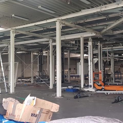 Baustelle mit Stahlträgern, Gerüsten und verstreuten Abfällen auf dem Boden.