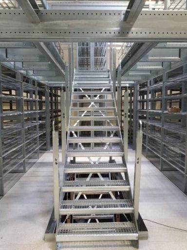 Blick auf eine Metalltreppe in einem Lager mit gestapelten Regalen.